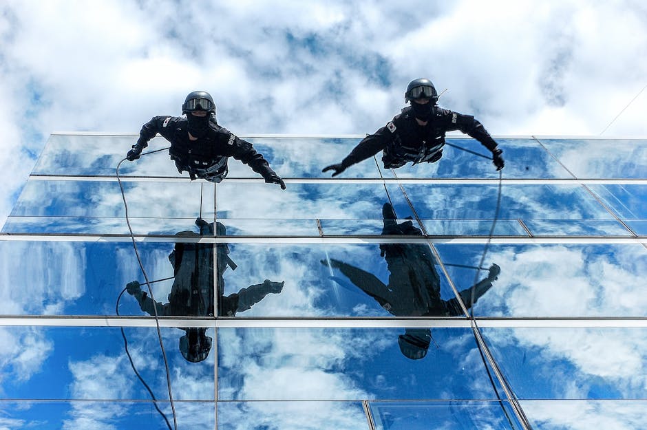 Gendarmerie officers rappelling down a glass building with sky reflections.